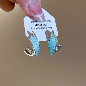 Detailaufnahme von versilberten Ohrringen mit hellblauen Kristallen.