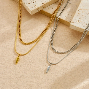 Detail view of gold and silver layered necklaces with spike pendants on stone slabs.