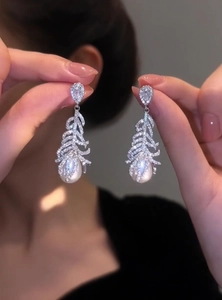 Detailed close-up showing micro-paved zircon feather earrings with elegant pearl drops.