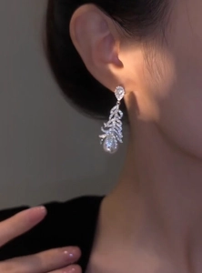 Macro view of elegant silver feather earrings featuring micro-pave stones and a pearl drop