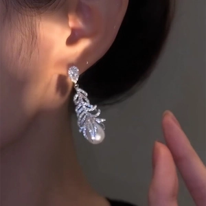 Detail view of an elegant feather-shaped earring with micro-set cubic zirconia and a pearl.