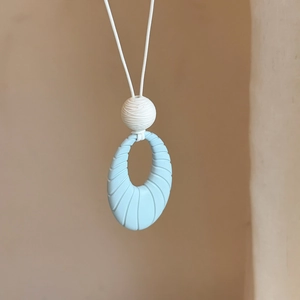 Close-up detail of a blue oval pendant necklace featuring an elegant textured shell pattern