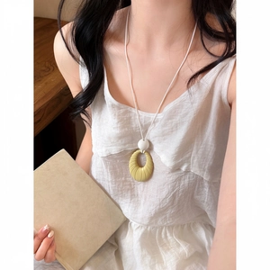 Close-up detail of a yellow oval pendant necklace with stripes on a white cord