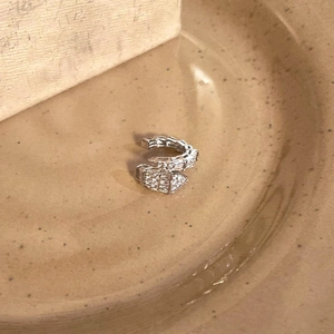 Macro view of a silver-toned zircon-paved snake ear cuff on a beige ceramic plate