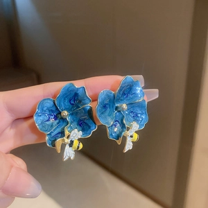 Nahaufnahme von eleganten blauen Blumenohrringen mit zarten Bienenanhängern und Goldrand