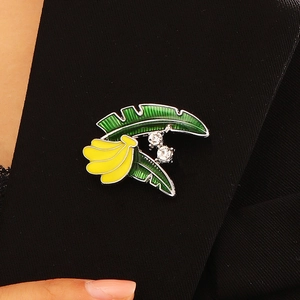 Detailansicht einer Emaille-Brosche mit grünen Bananenblättern und gelben Früchten auf Blazer.