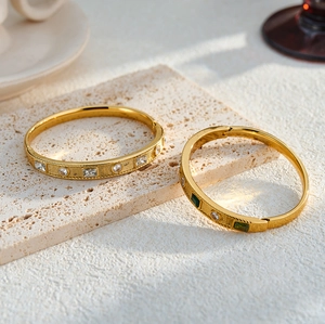 Close-up of gold stainless steel bracelets with geometric white and green zircon inlay.