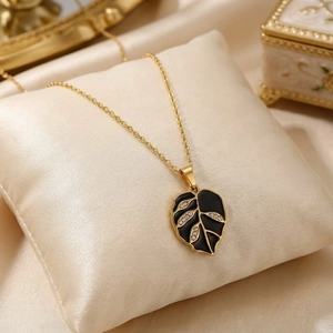 Close-up of gold leaf pendant necklace with black enamel finish and sparkling crystals.