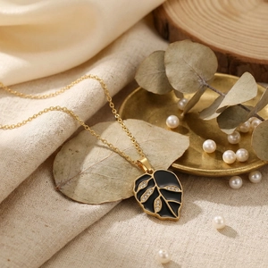 Close-up detail of a gold leaf pendant featuring black enamel and sparkling rhinestones
