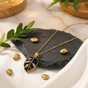 Detailed view of gold leaf pendant with black enamel and sparkling rhinestones on slate.