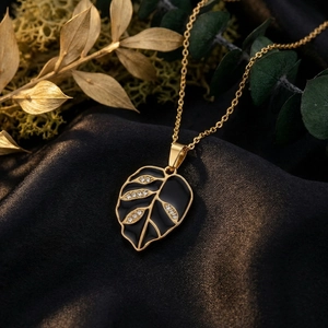 Close-up of gold leaf pendant with black enamel and rhinestones on dark fabric.