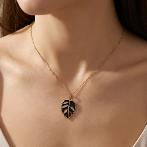 Close-up view of a gold-plated stainless steel necklace with a black enamel leaf pendant.