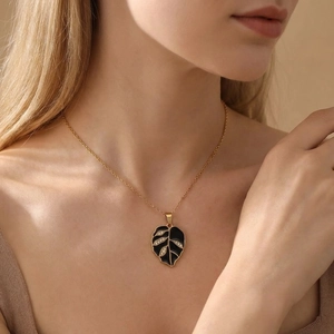 Close-up of elegant leaf pendant necklace featuring black enamel and rhinestones on model neck