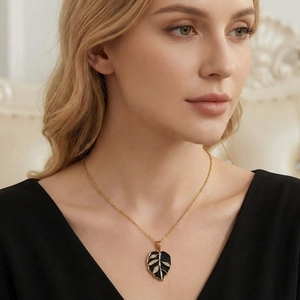 Elegant gold necklace with a black enamel leaf pendant and rhinestones worn by a model.