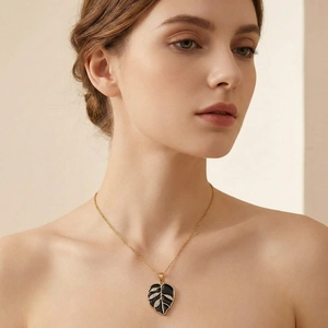 Detail of a black enamel leaf pendant necklace with crystals worn by a model.