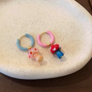 Detalle de pendientes de aro de hongo asimétricos sobre un plato de cerámica blanca.