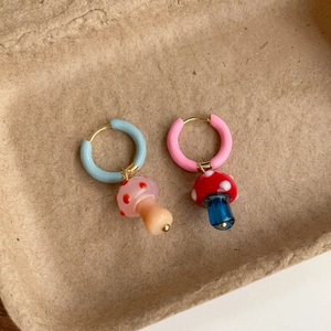 Primer plano de pendientes asimétricos de aro con hongos esmaltados estilo dopamina.