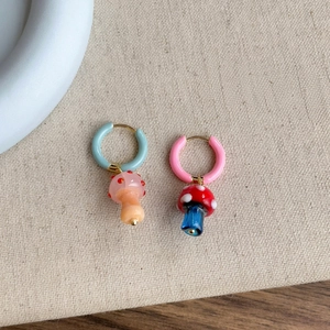 Detalle de pendientes de aro asimétricos con dijes de setas de colores.