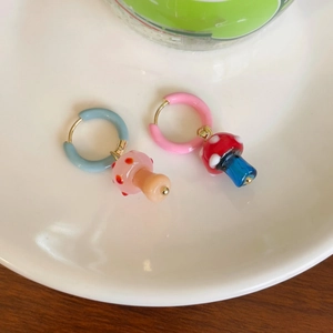 Detalle de pendientes de aro asimétricos con dijes de hongo de esmalte en un plato blanco