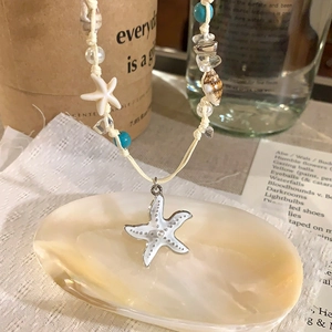 Detailed macro shot of a white starfish pendant on a beaded shell woven beach choker necklace.