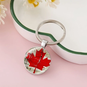 Close-up of a Canada flag maple leaf keychain on a pink background with daisies