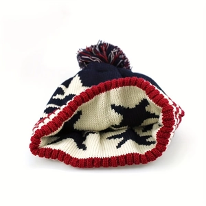 Detail of navy knit beanie with white stars, pom-pom, and red ribbed hem edges