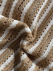 Close-up of brown and white striped crochet knit fabric showing detailed hollow textures