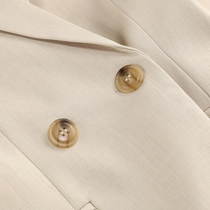 Gros plan détaillé des boutons en résine ambrée et de la texture sergé d'un blazer beige
