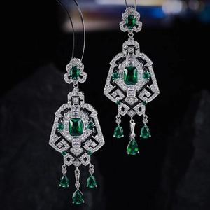 Detailed close-up of emerald drop earrings with sparkling zircon stones on dark stone background