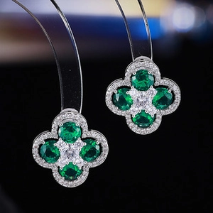 Macro shot of silver four-leaf clover earrings with green emerald stones and zircon detailing