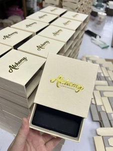 Detail showing beige sliding jewelry box with gold logo and black sponge insert