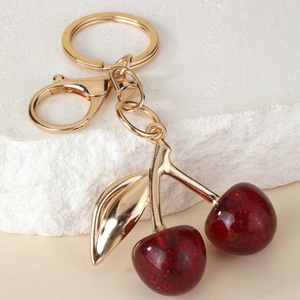 Fashionable cherry keychain with red resin fruit and gold metal leaf on white stone background