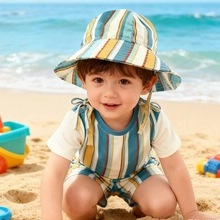 Cute toddler boy playing on a beach wearing a striped cotton sun hat and matching romper