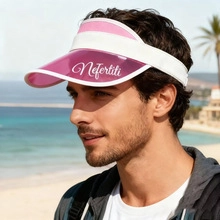 Model wearing a pink transparent sun visor with Nefertiti text at a sunny beach