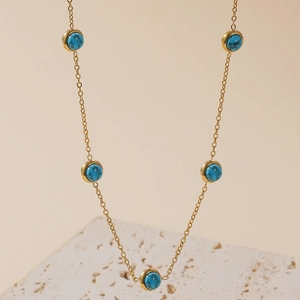 Minimalist gold necklace with five round turquoise stones on a textured stone background