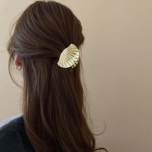 Golden shell-shaped metal hair claw clip shown from the back on curly brown hair