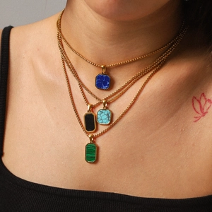 Close-up of stacked gold box chains with natural stone pendants in blue, green, and black