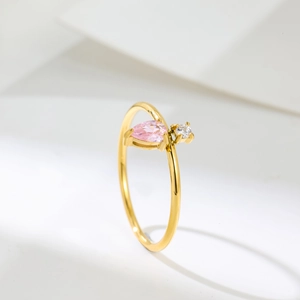 Close-up of golden ring featuring pear-shaped pink stone and round white zircon detail