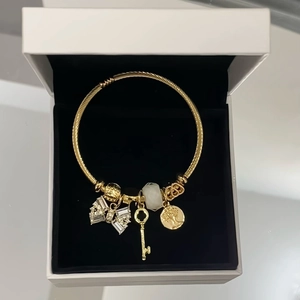 Golden stainless steel bangle with crystal bow, key, and tree charms in a jewelry box