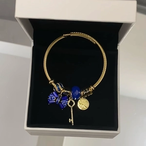 Detail of gold open bangle with blue bow charm, key pendant and tree of life medallion
