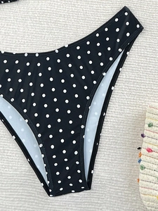 Dettaglio slip bikini nero a pois con taglio sgambato su un tappeto da spiaggia intrecciato