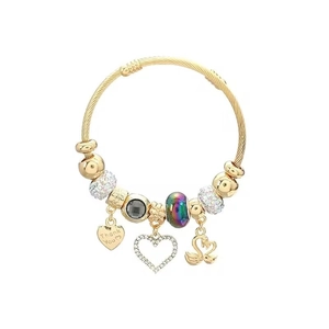 Detail of golden twisted wire bracelet with swan, heart charms and colorful beads