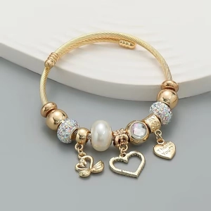 Detail of golden cable cuff bracelet featuring pearl, heart, and swan charms
