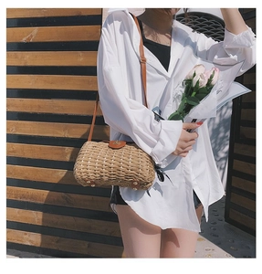 Detail of beige straw bag showing leather strap, gold base studs and woven texture