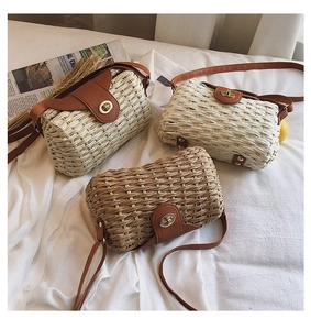 Detailed view of woven straw bags in beige and tan with leather straps on a white fabric