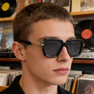 Détail de lunettes de soleil carrées avec monture noire et branches dorées sur modèle