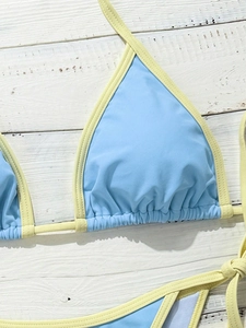 Close-up of color-block bikini set with blue fabric and yellow trim on white wood board