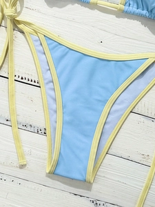 Detail of color-block bikini bottom with light yellow side ties on blue fabric