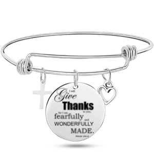 Close-up of adjustable silver bangle featuring scripture charm, cross and heart pendants