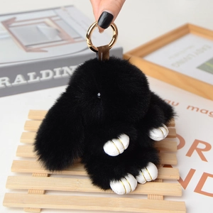 Detailed macro view of black plush rabbit keychain with gold clasp and white leather paws